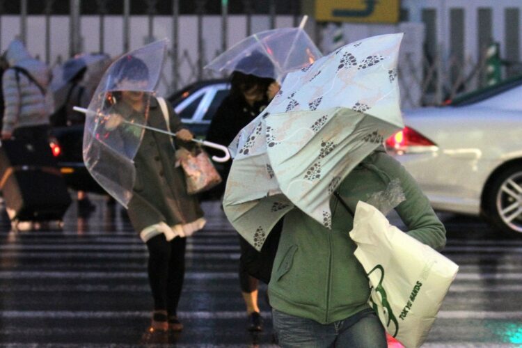 台風並みの暴風と雨の中、傘を差して歩く人々（写真／2012年4月、時事通信フォト）