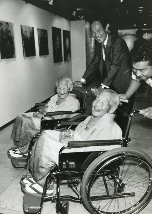 幸男さんが押す車いすに乗るきんさん（奥）は107才、ぎんさんは108才まで天寿を全うした（写真は1992年）