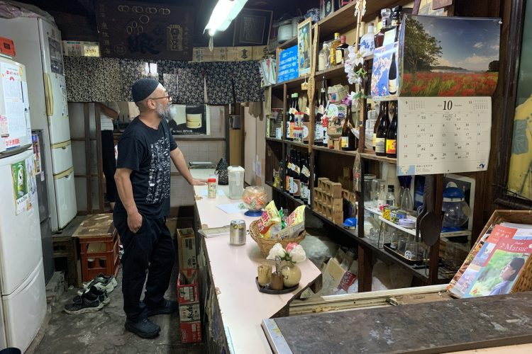 カウンターと後ろに酒が入った冷蔵庫が配置された魚住酒店の店内