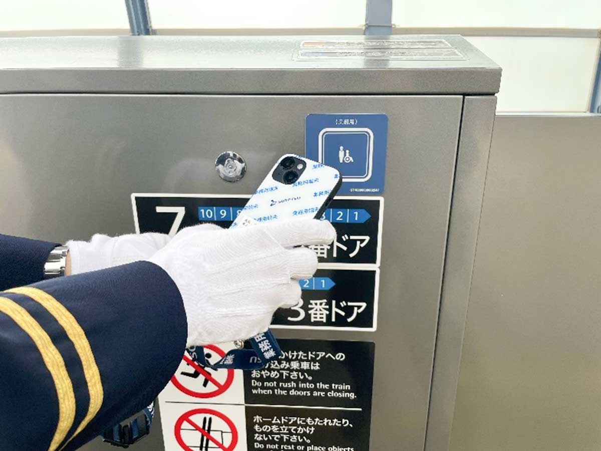 ホームドアに設置されたNFCにスマートデバイスをかざす駅係員。ヒューマンエラーを防ぐため、移動制約者の乗車位置入力を自動化した。画像提供：日立製作所
